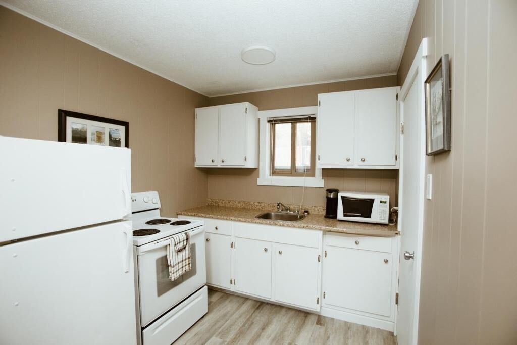 A compact kitchen with white cabinets, a stove, a microwave, and a window.