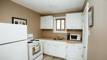 Une cuisine de taille réduite, avec des meubles blancs, une cuisinière, un four à micro-ondes et une fenêtre.