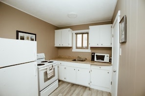 A compact kitchen with white cabinets, a stove, a microwave, and a window.