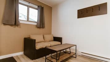 Um quarto com um sofá marrom, uma mesa de centro de madeira, uma janela com cortinas e um cabideiro fixado na parede.