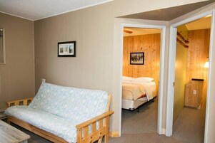 Una habitación con un banco de madera, una cama con colchón blanco y una pared de madera con un cuadro enmarcado.
