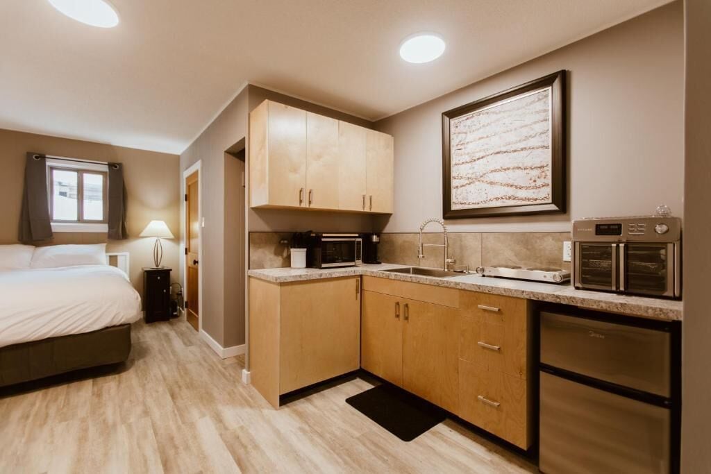 A compact hotel room with a bed, a kitchenette, a microwave, a refrigerator, and a framed artwork on the wall.
