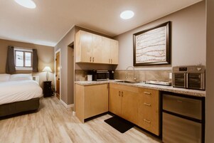 Habitación de hotel compacta con cama, kitchenette, microondas, refrigerador y una obra de arte enmarcada en la pared.
