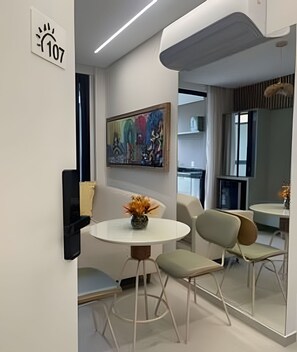 Ein modernes Hotelzimmer mit einem runden Esstisch, zwei Stühlen, einem Bild an der Wand und einem großen Spiegel, der den Raum reflektiert.