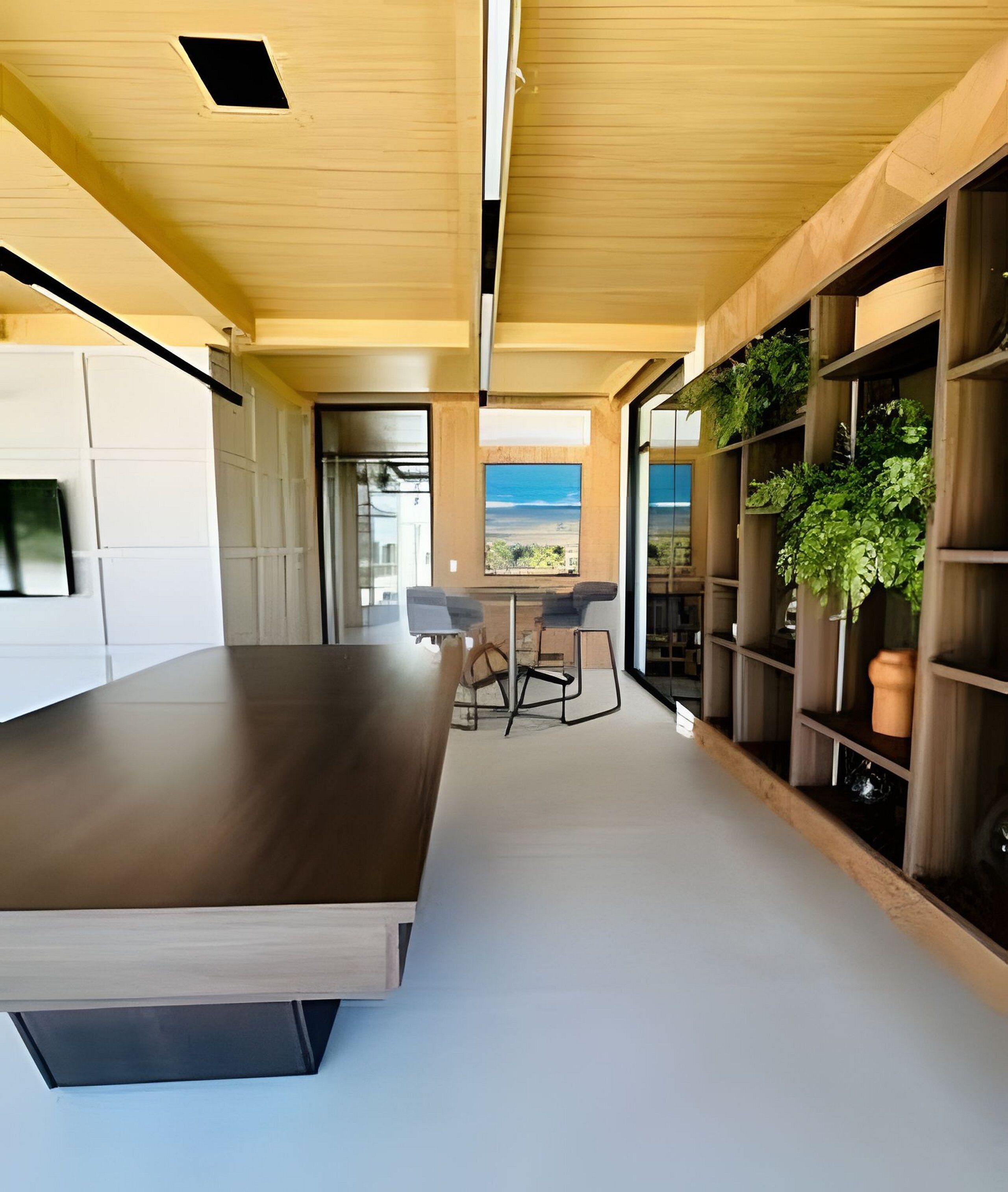 A modern kitchen with a large island, built-in shelving with plants, and a view of the sea.