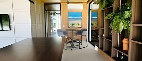 A modern kitchen with a large island, built-in shelving with plants, and a view of the sea.