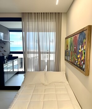 Ein modernes Schlafzimmer mit einem großen Bett, einem Gemälde an der Wand und Blick aufs Meer durch das Fenster.