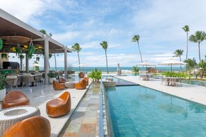 Ein Poolbereich mit Liegestühlen, einer Bar und Blick auf den Ozean.