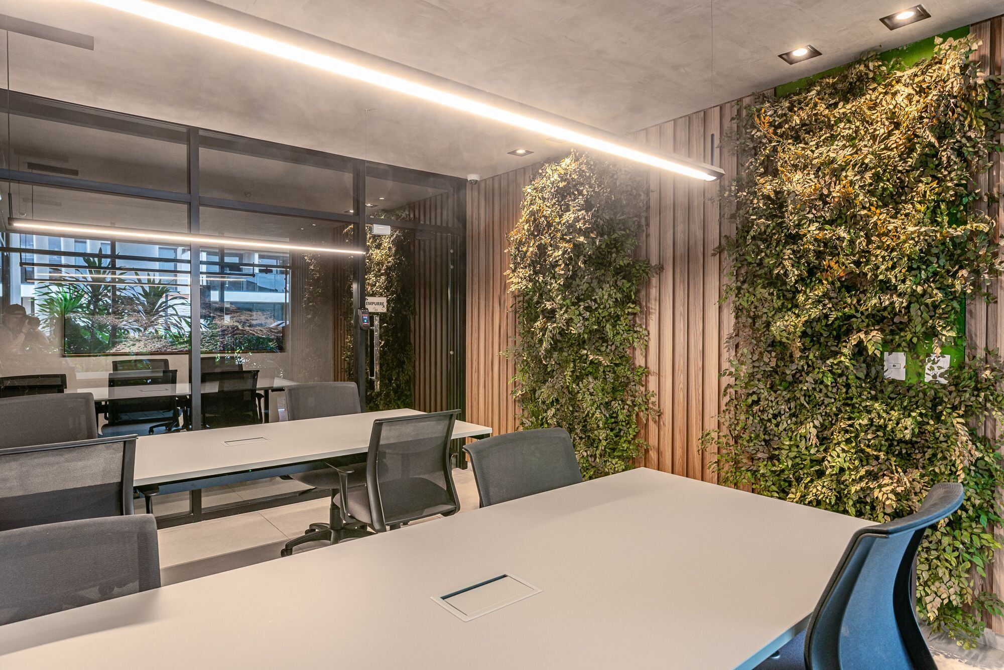 A conference room with a long table, several chairs, and a wall covered in greenery.