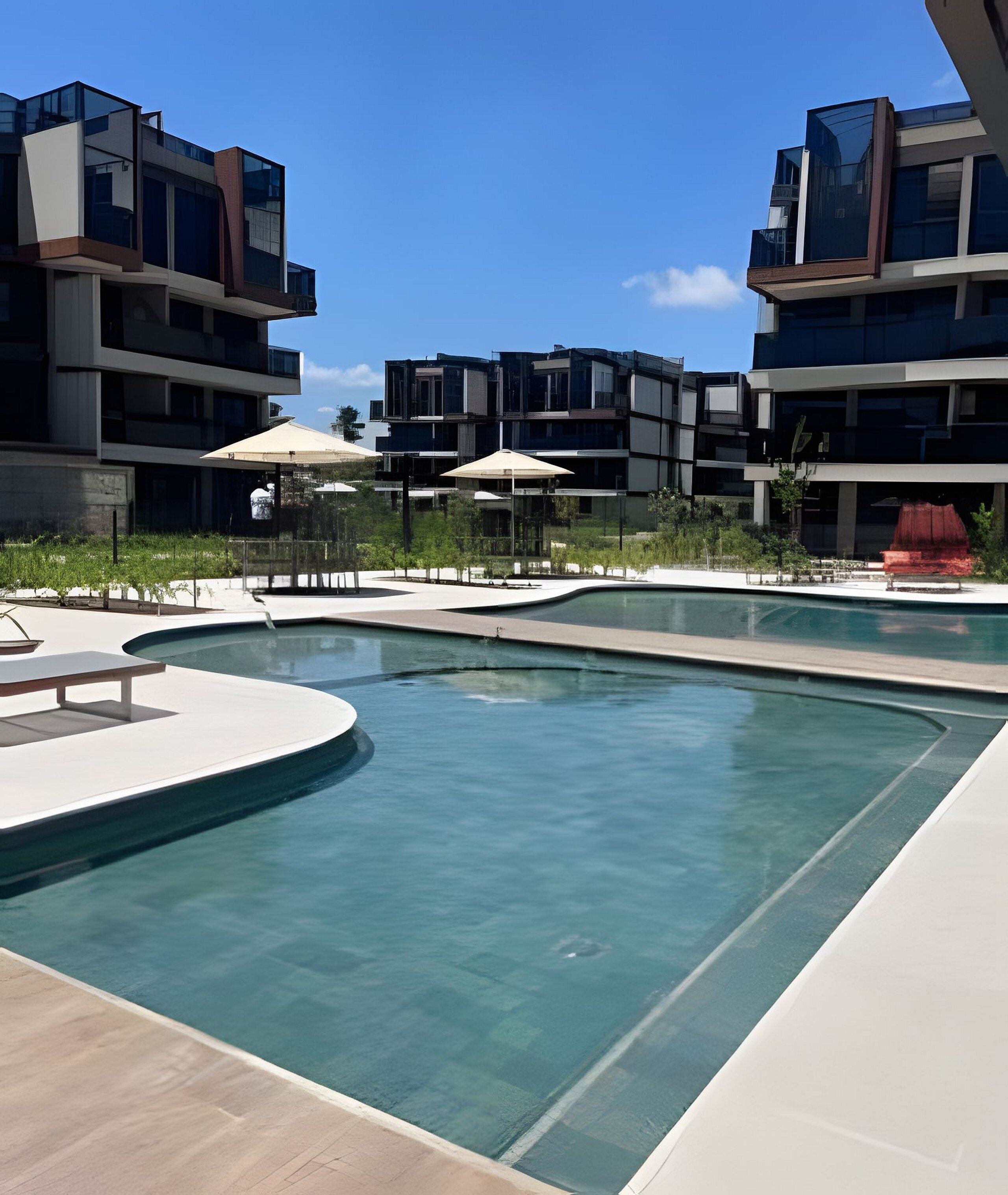 A modern outdoor swimming pool area with multiple pools, surrounded by contemporary buildings and outdoor seating.