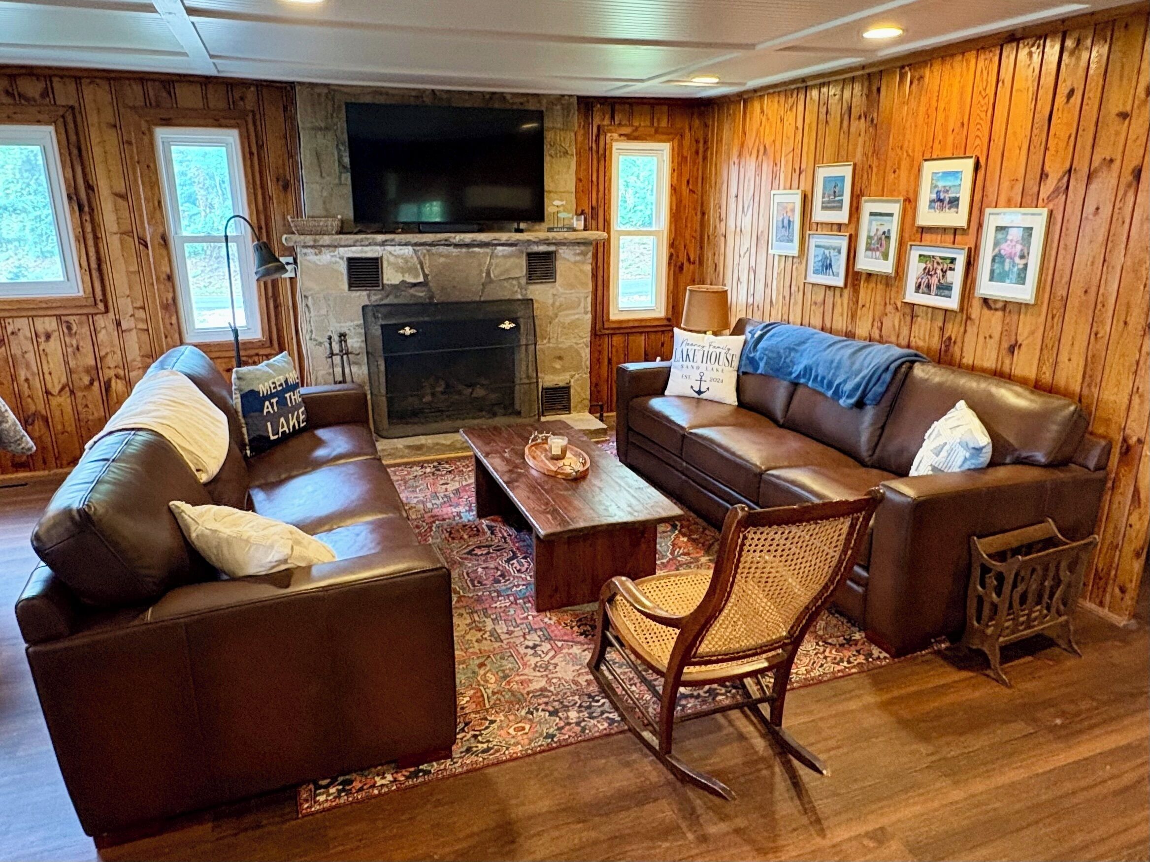 A cozy living room with a stone fireplace, leather sofas, a wooden coffee table, and a television mounted above the fireplace.