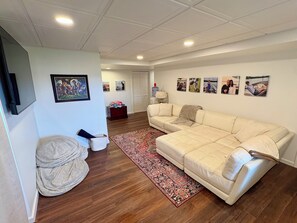 Ein Wohnzimmer mit einem beigefarbenen Ecksofa, einem gemusterten Teppich und einer Wand mit gerahmten Fotos.