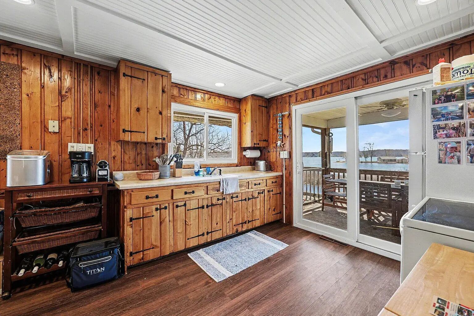 A wooden cabin kitchen with a large island, wooden cabinets, and a sliding glass door leading to an outdoor deck.