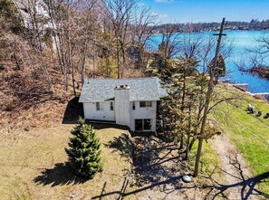 A two-story house with a sloped roof, surrounded by trees and a body of water. - Lakefront home combining old school warmth and charm with clean, modern updates! (Onsted)