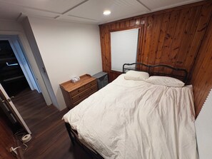 Ein Schlafzimmer mit einem hölzernen Kopfende, einem Bett mit weißer Bettwäsche, einem Nachttisch und einem Fenster mit Jalousien.