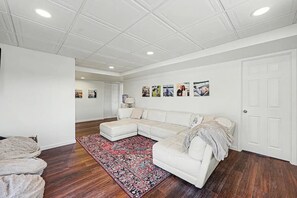 Un salon avec un canapé d’angle, un tapis à motifs et une porte dotée d’un cadre blanc.