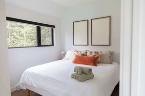 Ein Schlafzimmer mit einem Bett, Kissen, einem Fenster und zwei an der Wand befestigten Bilderrahmen.