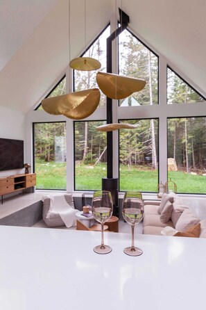 A modern living room with a large window, a sofa, and two wine glasses on a table.