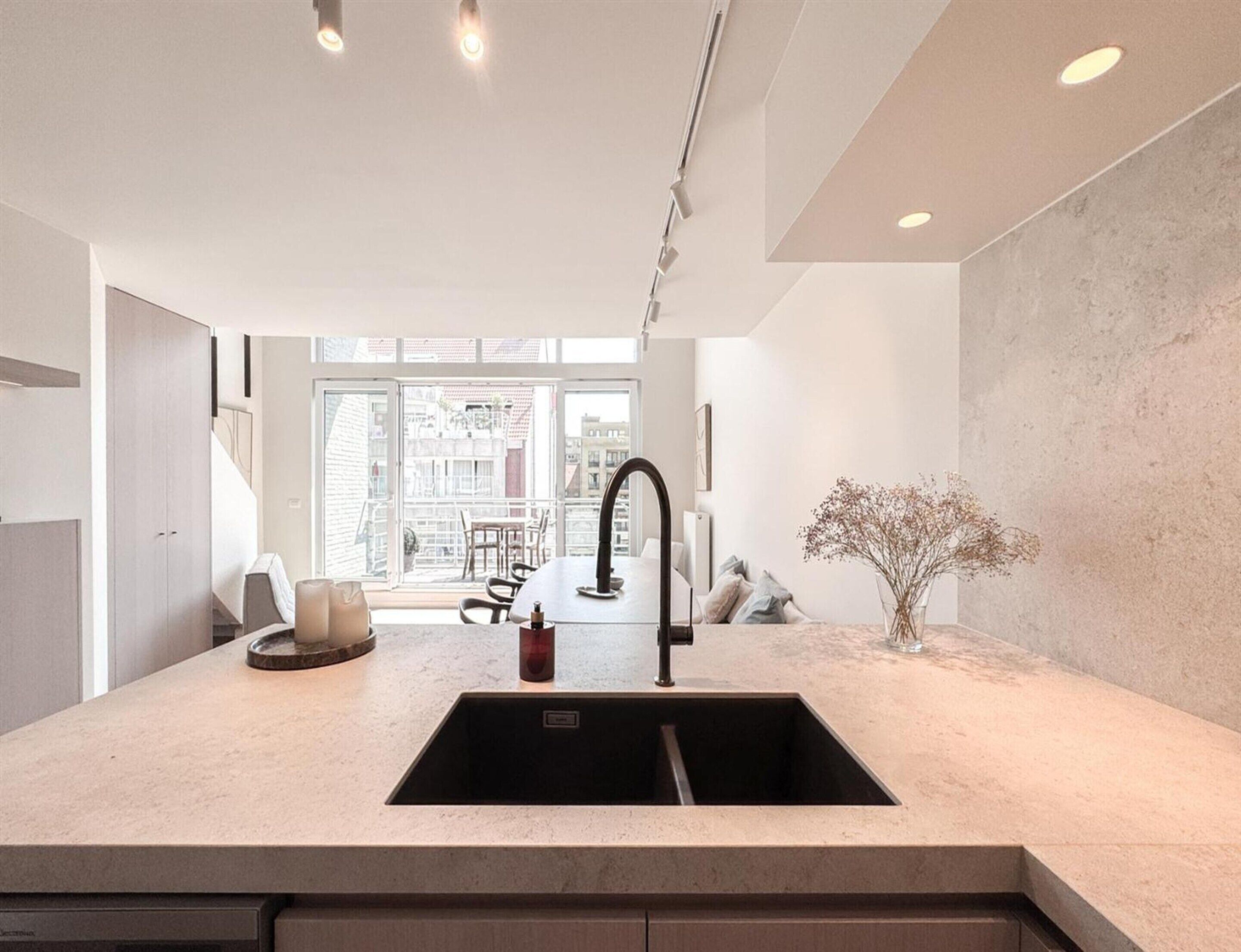 Cocina moderna con un lavamanos central, zona de comedor con sillas y vistas a la ciudad a través de amplios ventanales.