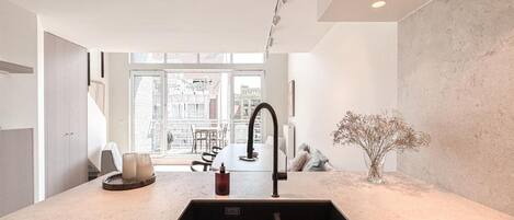 A modern kitchen with a central sink, a dining area with chairs, and a view of the cityscape through large windows.