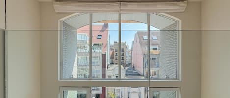 A room with a large window overlooking a cityscape, a balcony with a table and chairs, and a modern interior design.