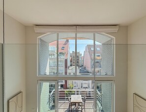 Een kamer met een groot raam met uitzicht op een stadsbeeld, een balkon met een tafel en stoelen, en een modern interieur.
