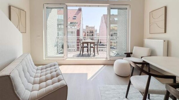A modern interior with a sofa, dining table, and chairs, large windows with a view of buildings. - Spacious Duplex in Knokke Centre (Knokke-Heist)
