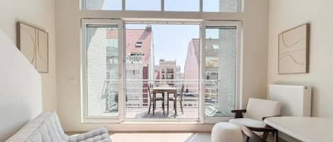 Un intérieur moderne avec un canapé, une table à manger et des chaises, de grandes fenêtres offrant une vue sur les bâtiments.