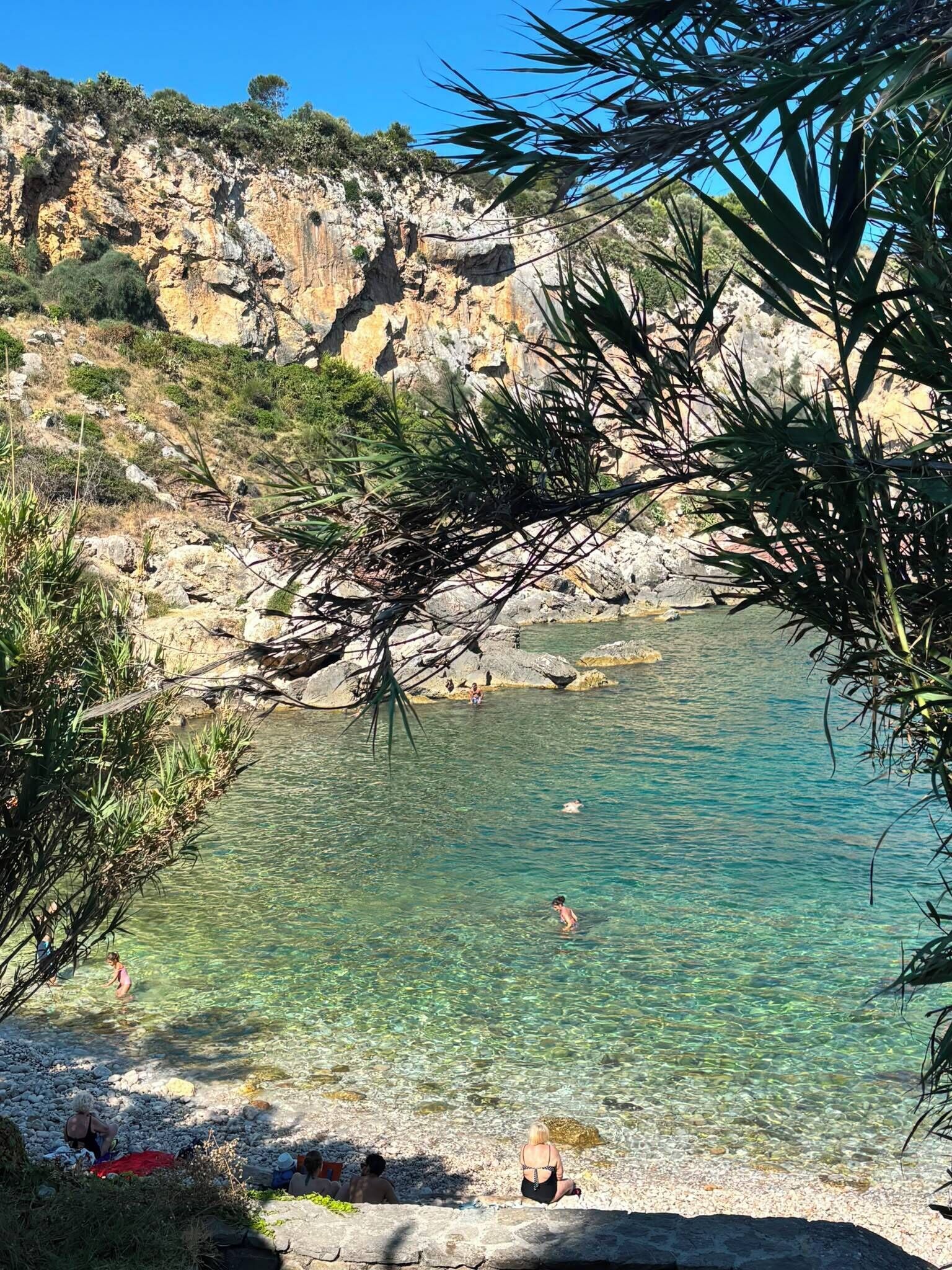 Ein sauberer Küstenstrand mit Felsen, klares Wasser und Menschen, die die Gegend genießen.