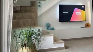 En modern inredning med en trappa, en platt-TV som visar RADIO ITALIA och en krukväxt.