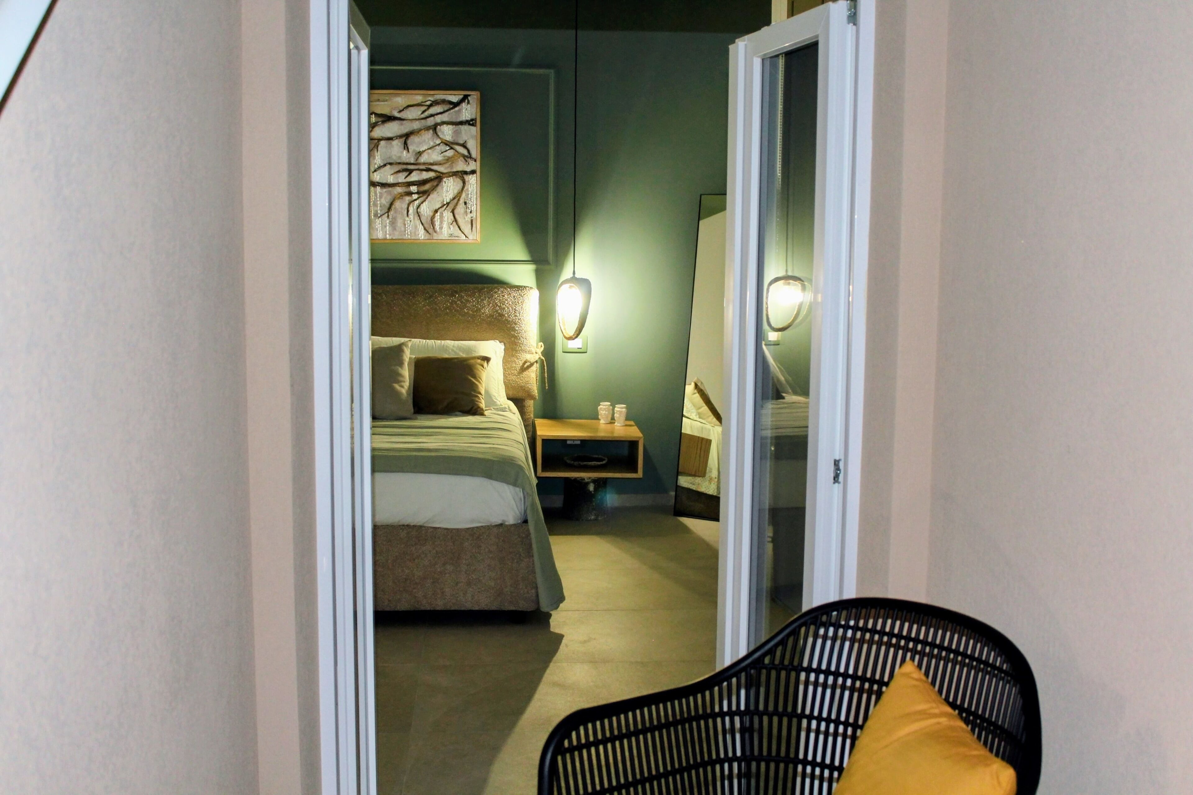 Una camera d'albergo con un letto, un comodino, una lampada e una sedia.