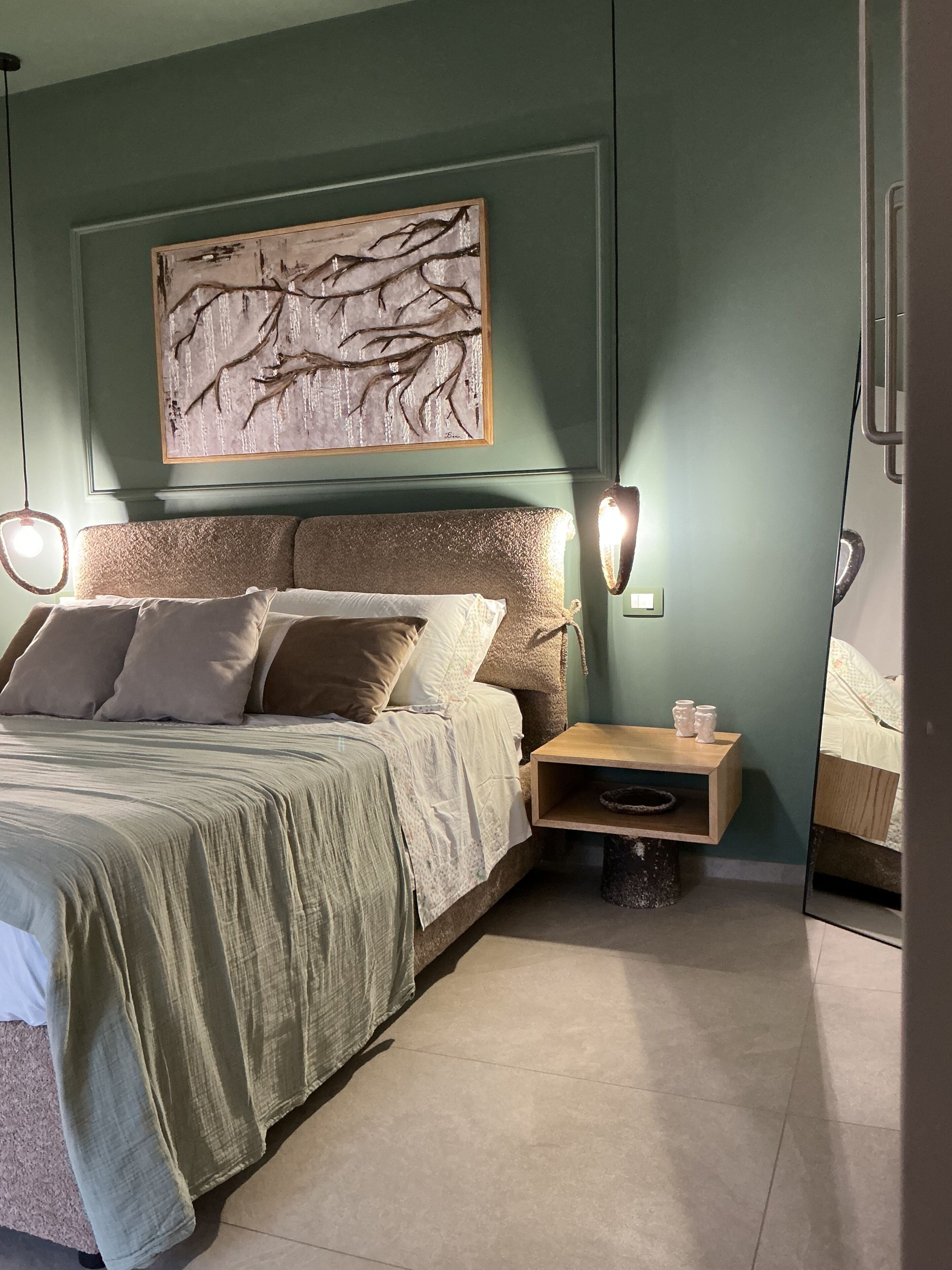 Um quarto com uma cama, mesas de cabeceira, uma obra de arte na parede e um espelho.