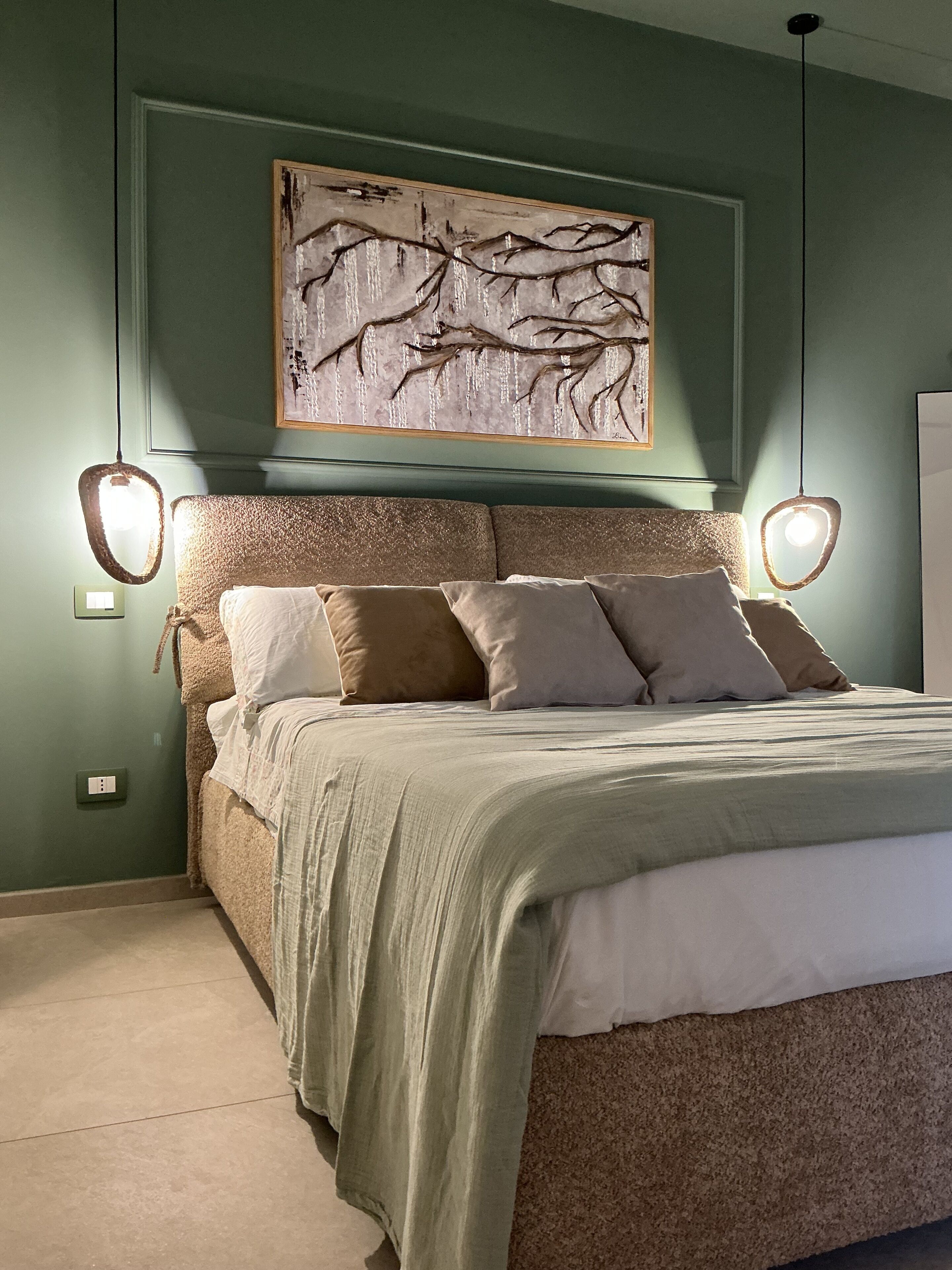 A bedroom with a bed, a wall-mounted artwork, and two wall sconces.