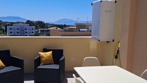En terrass med ett bord och stolar, en whiteboard och utsikt över byggnader och berg.