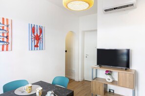 Ein modernes Wohnzimmer mit Flachbildfernseher, einem Essbereich mit Tisch und Stühlen sowie Kunstwerken an den Wänden.