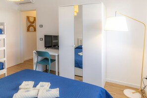A hotel room with a bed, a desk, a chair, a TV, and a lamp.