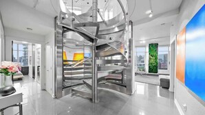 Un interior moderno con una escalera espiral central, un ventanal con vistas a la ciudad y un diseño minimalista.