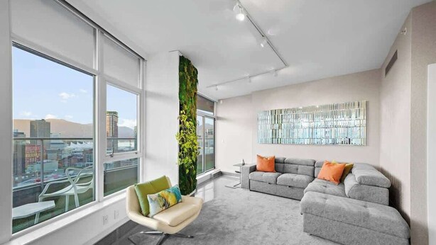 Una sala de estar moderna con un ventanal grande, un sofá modular gris, un sillón blanco y un jardín vertical.