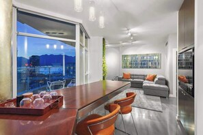 Ein modernes Wohnzimmer mit großem Fenster, einem Essbereich mit Holztisch und einer grauen Sofagarnitur.