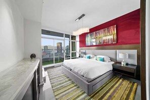 Ein modernes Hotelzimmer mit einem großen Bett, einer roten Akzentwand und Blick auf die Stadt.