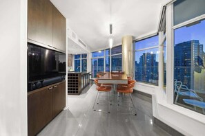 Een moderne keuken met een grote televisie, een eethoek met stoelen en grote ramen met uitzicht over de stad.