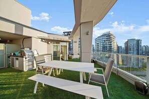 Eine Dachterrasse mit Grill, Sitzgelegenheiten und Blick auf die Stadtlandschaft.
