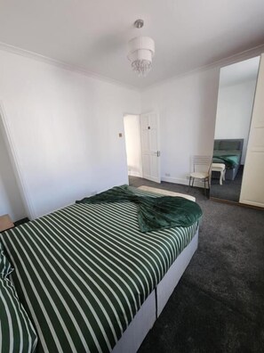 Een slaapkamer met een bed, een stoel, een bureau en een spiegel.