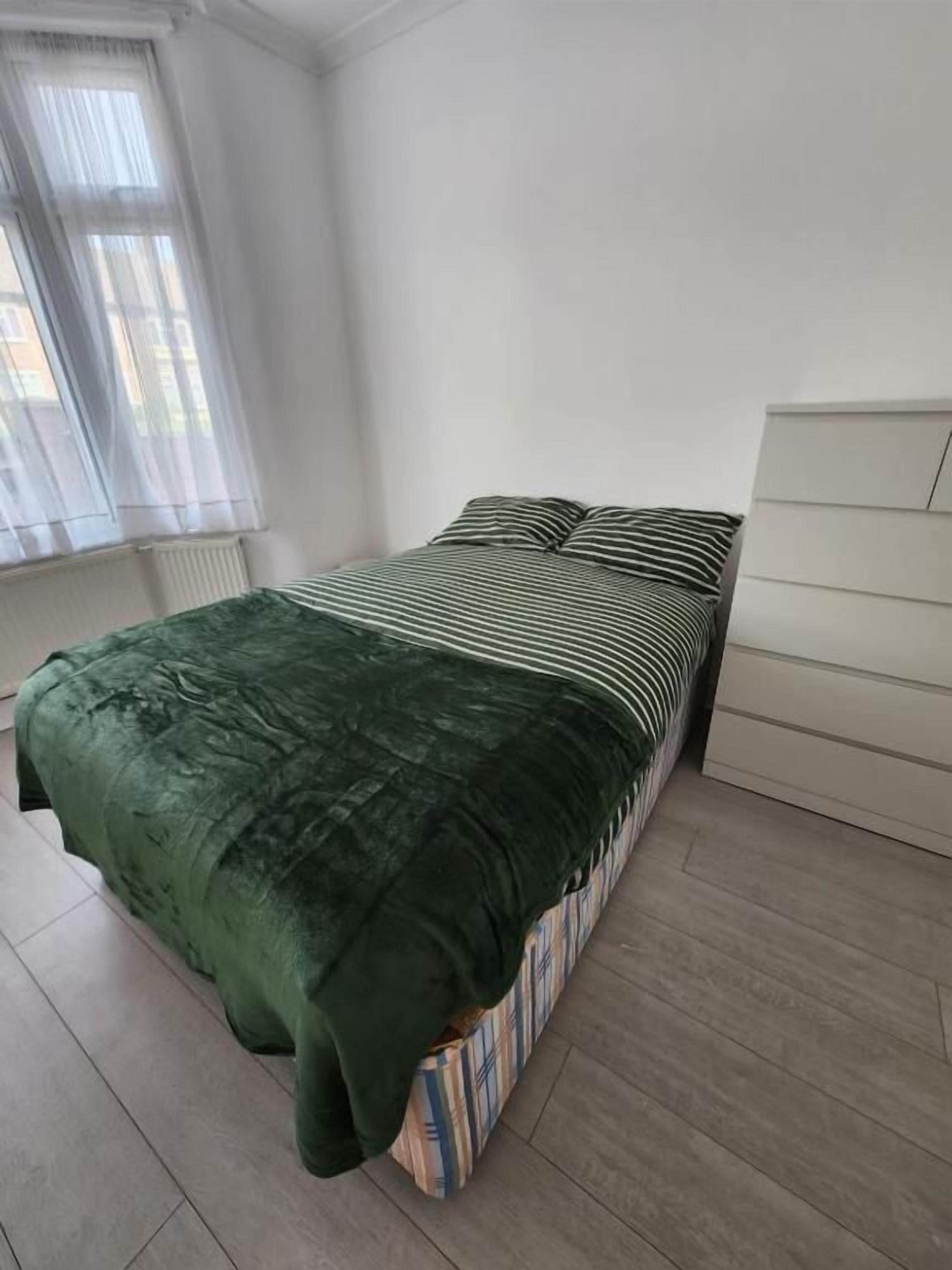 Un dormitorio con cama, ventana con cortinas traslúcidas y radiador.