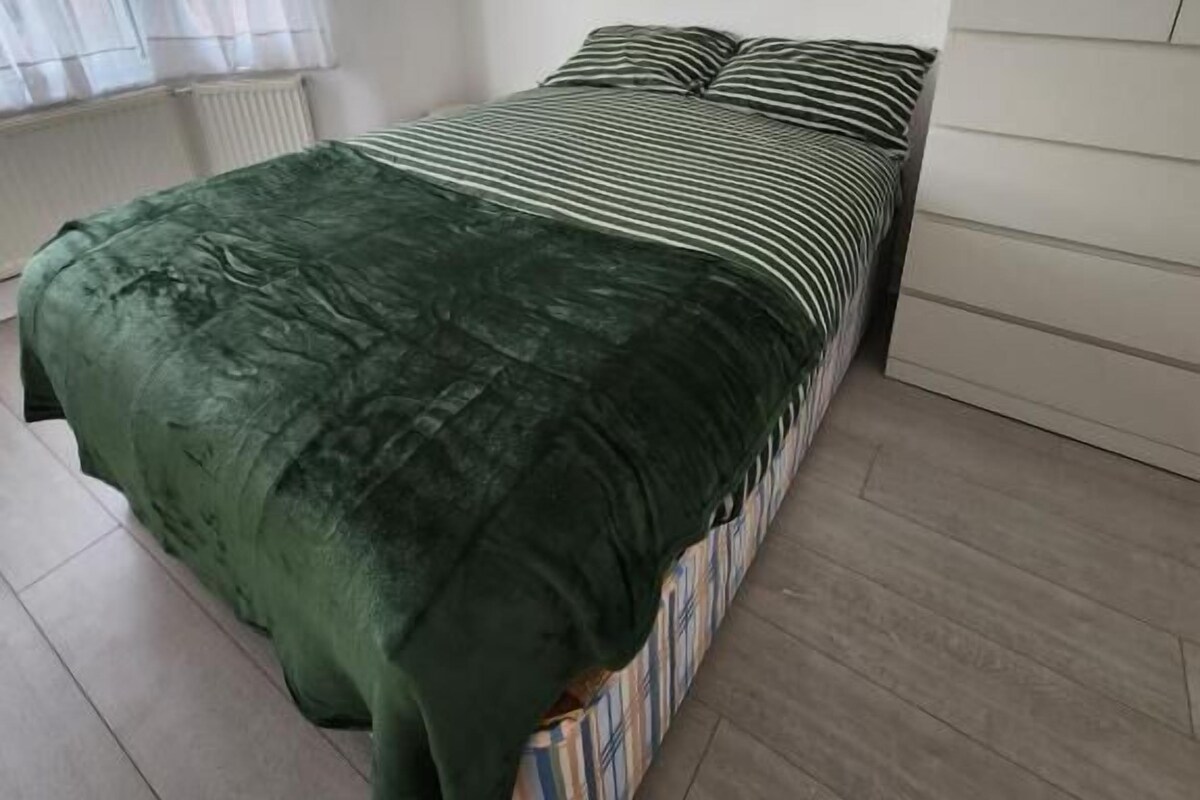 Ein Schlafzimmer mit einem Bett, einem Fenster mit leichtem Vorhang und einer Heizung.