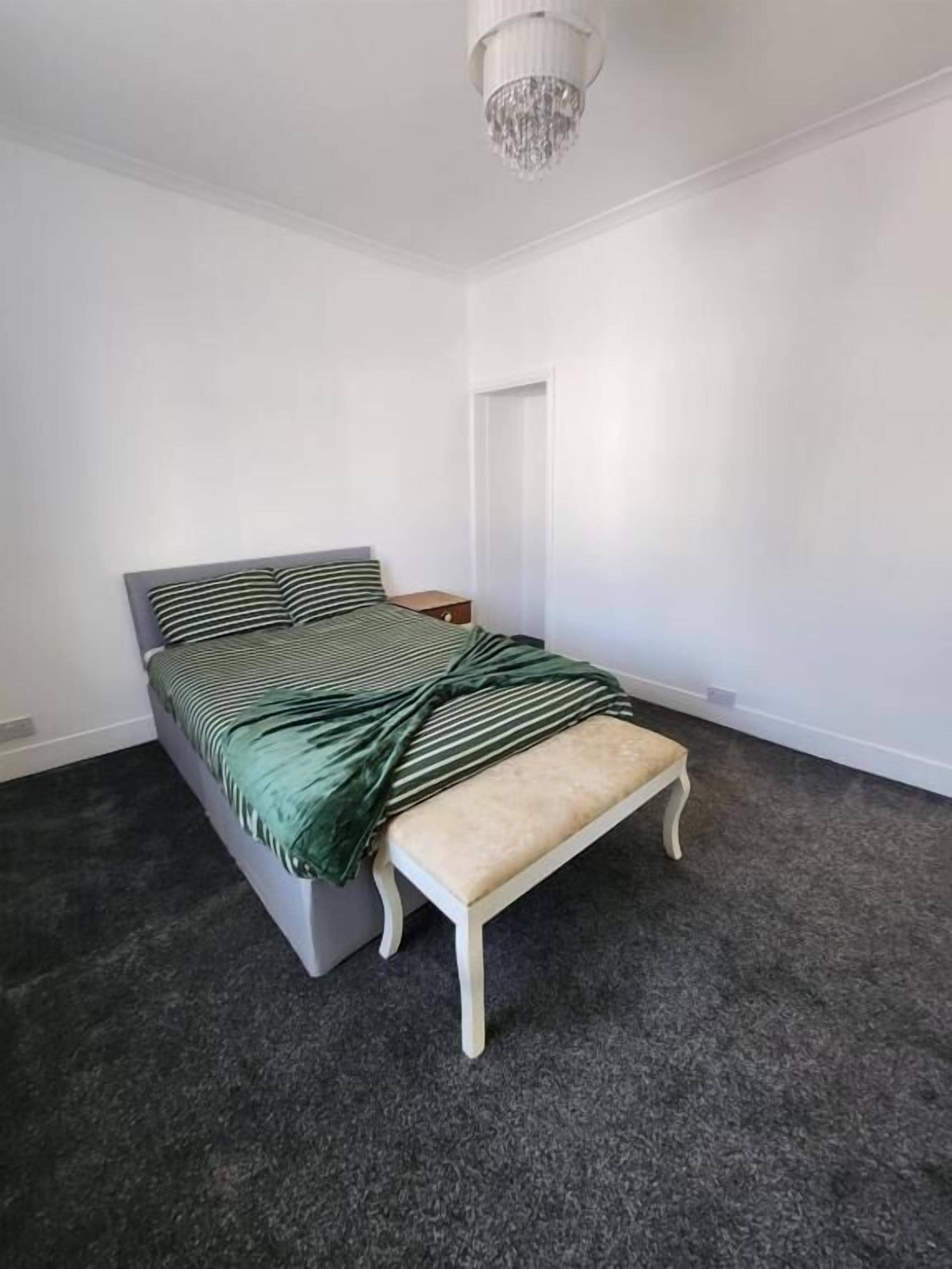A bedroom with a bed, a bench, a door, and a chandelier.