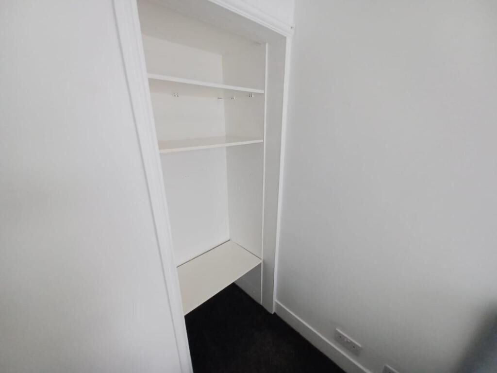 Un armario blanco con puertas abiertas, mostrando estantes y un espacio inferior.