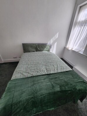 A room with a bed, a window with sheer curtains, and a carpeted floor.