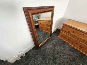Ein Zimmer mit einem hölzernen Schminktisch, einem Spiegel mit Zierrahmen und Teppichboden.