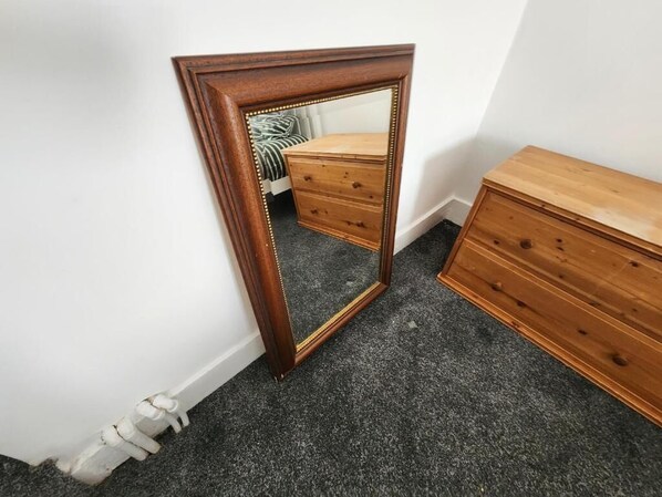 A room with a wooden dresser, a mirror with a decorative frame, and a carpeted floor.